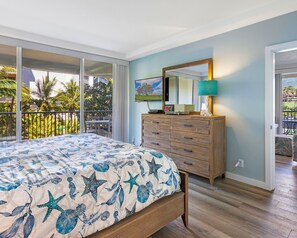 Quarto com cama, cômoda, televisão e varanda com vista para palmeiras.