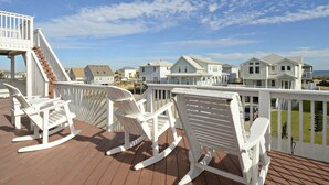 A wooden deck with white rocking chairs and a white railing overlooking a residential area with houses and a clear sky. - KH4004- Oceanside-5 BRs, Elevator, Pool Table, Private Pool and Hot Tub! (Kitty Hawk)