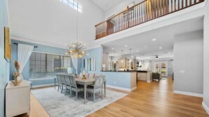 A spacious dining area with a high ceiling, a staircase to an upper level, and a kitchen in the background. - Polished Villa with Home Theater at Reunion (Kissimmee)
