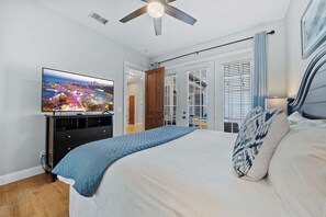 Une chambre à coucher avec un lit, un téléviseur posé sur une commode, un ventilateur de plafond et une vue sur le paysage urbain par la fenêtre.
