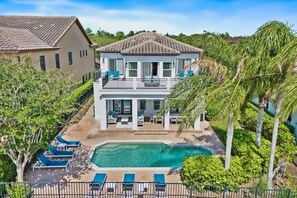 Une maison à deux étages avec une piscine, entourée de palmiers et d’un jardin bien entretenu.