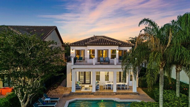 A two-story house with a balcony, a swimming pool, and outdoor seating. - Polished Villa with Home Theater at Reunion (Kissimmee)