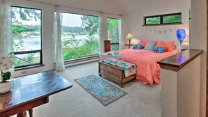Una camera da letto con un letto, un comodino, una cassettiera e una finestra vista foresta e lago.