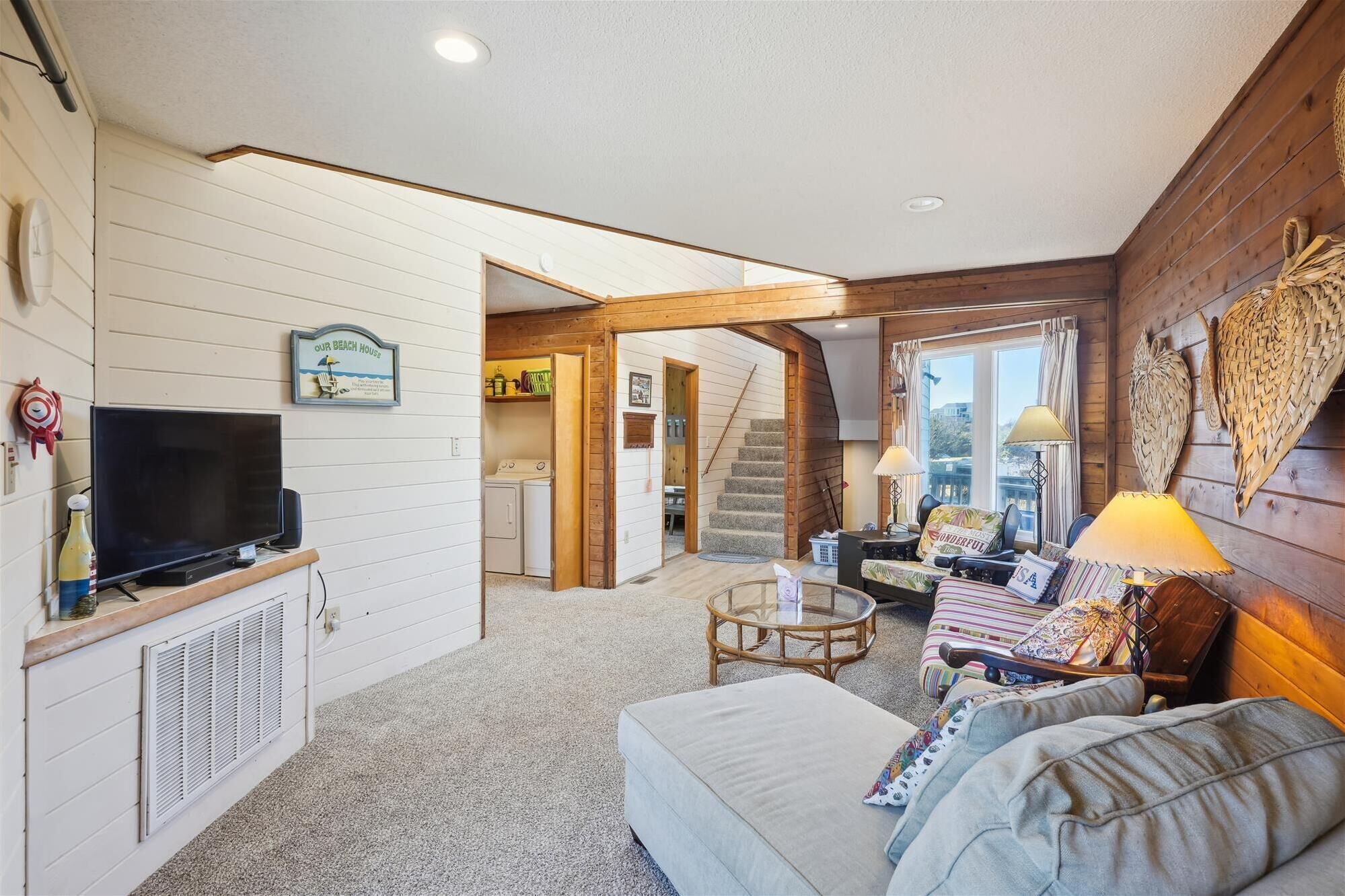A cozy living room with a television, a sofa, a coffee table, and a staircase leading to another room.