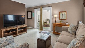 A living room with a flat-screen TV, a wooden entertainment unit, a sofa, a coffee table, and a sliding glass door leading to a balcony. - Comfortable Townhome with a Short Walk to Community Pool and the Beach! (Miramar Beach)