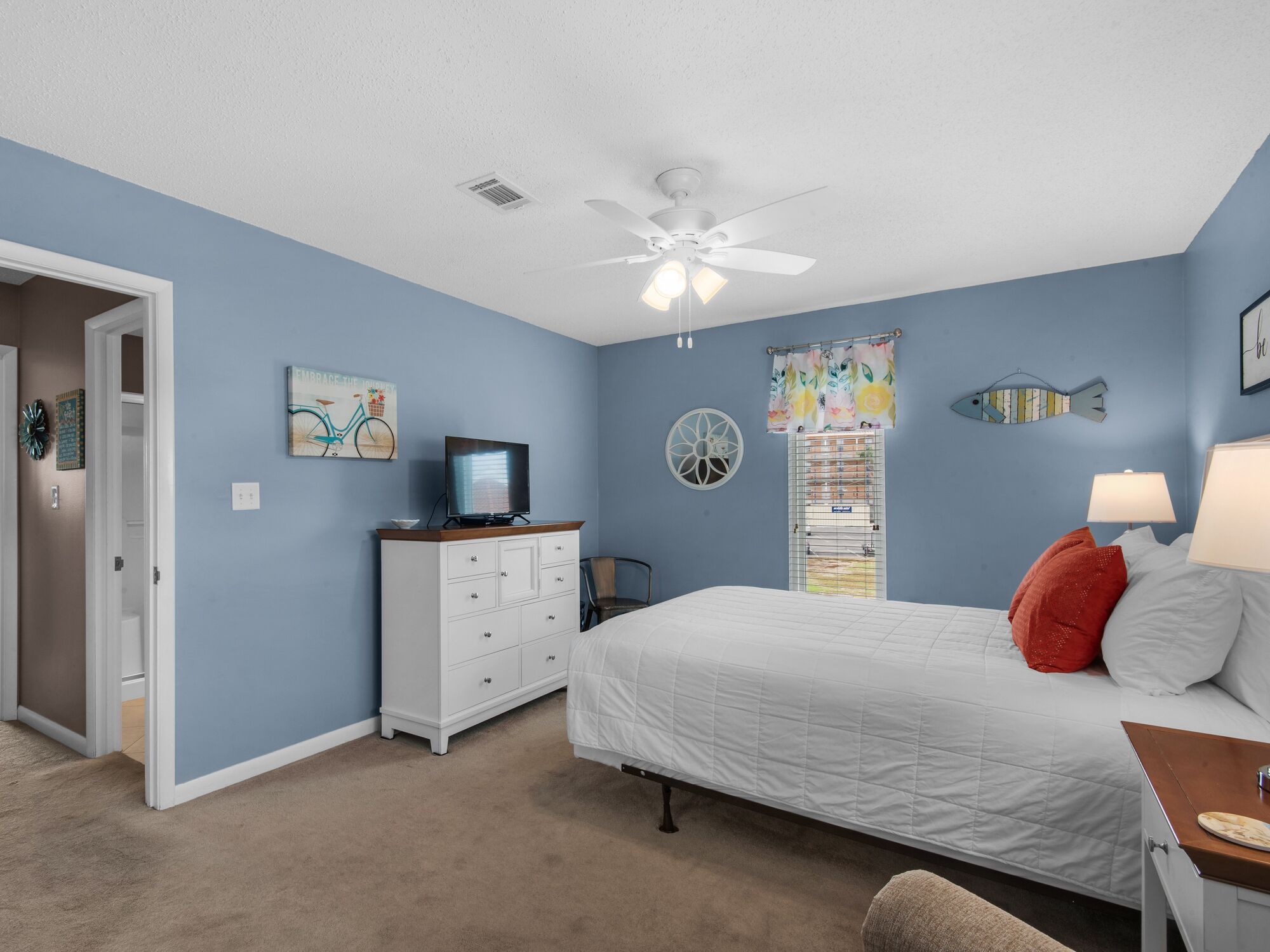 A bedroom with a bed, dresser, ceiling fan, and artwork on the walls.