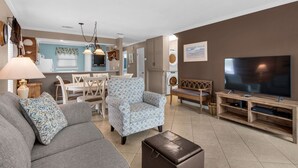 A living room with a sofa, armchair, ottoman, TV, and a dining area with a table and chairs. - Comfortable Townhome with a Short Walk to Community Pool and the Beach! (Miramar Beach)