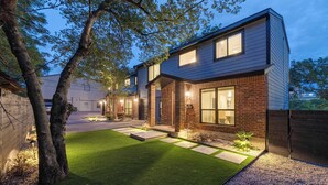 A modern two-story house with a well-maintained lawn, a brick exterior, and a gated driveway. - Designer Duplex | Pool, Fire Pit, Near UT Football (Austin)