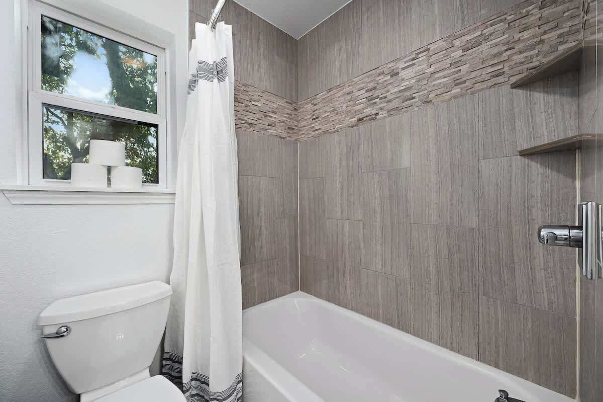 Ein Badezimmer mit Dusche, Toilette und einem Fenster mit Blick auf Bäume.