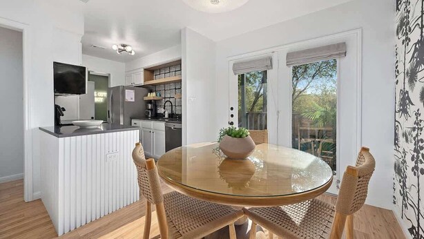 Een moderne keuken met witte kasten, een centraal eiland en een eetgedeelte met een glazen tafel en geweven stoelen.