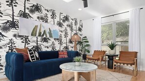 A living room with a blue sofa, a glass coffee table, and a patterned wall. - Designer Duplex | Pool, Fire Pit, Near UT Football (Austin)