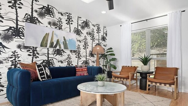 A living room with a blue sofa, a glass coffee table, and a patterned wall. - Designer Duplex | Pool, Fire Pit, Near UT Football (Austin)
