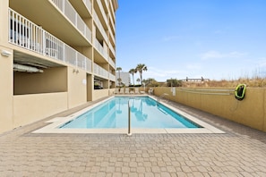 Une piscine avec une terrasse carrelée, un bâtiment doté de balcons et des palmiers en arrière-plan.