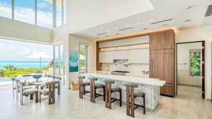 Une cuisine moderne dotée d’un grand îlot central, de tabourets de bar et offrant une vue sur l’océan.