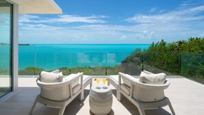 Un balcon avec deux fauteuils en osier et une petite table ronde, d’où l’on peut admirer une mer turquoise et un ciel dégagé.