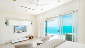 Une chambre d’hôtel moderne dotée d’un grand lit, d’un coin salon avec des fauteuils, d’une télévision à écran plat, d’un ventilateur de plafond et d’un balcon offrant une vue sur l’océan.
