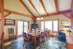 A dining area with a wooden table and chairs, a chandelier, and large windows.