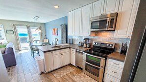 A modern kitchen with white cabinets, stainless steel appliances, and a wooden floor. - Unwind in Style at Elysium (Surf City)