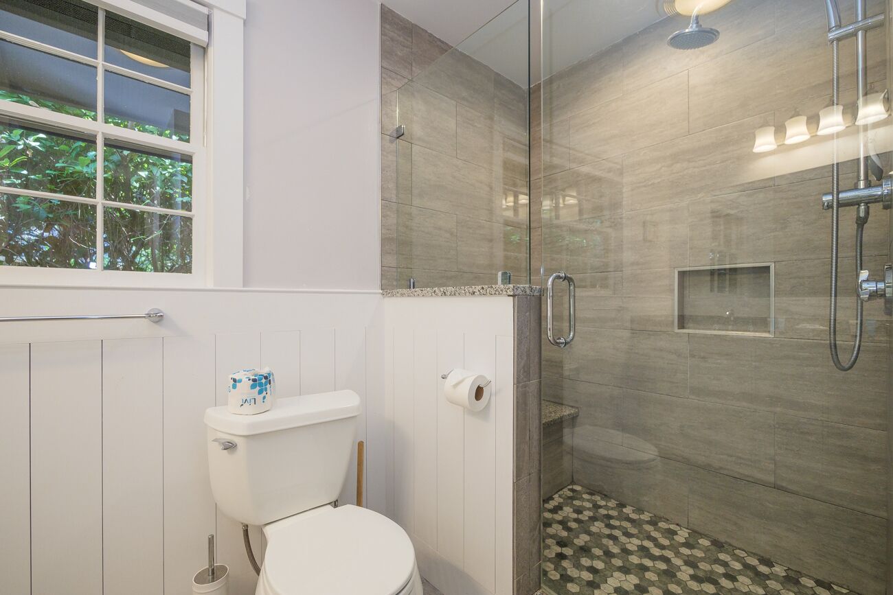 A modern bathroom with a glass-enclosed shower, a toilet, and a window with a view of greenery.