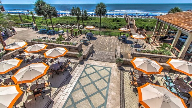 Terraza en la azotea con mobiliario exterior y sombrillas, con vistas a una playa y al océano.