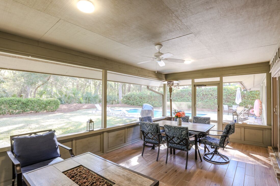 A covered patio with a table and chairs, large windows, and a ceiling fan.