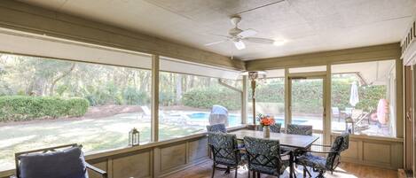 A covered patio with a table and chairs, large windows, and a ceiling fan.