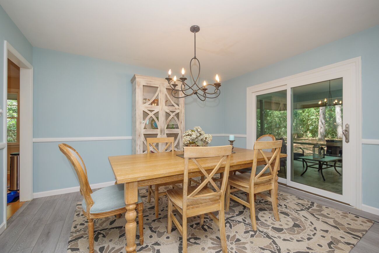 A dining area with a wooden table and chairs, a chandelier, and a view through glass doors.