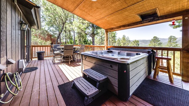 A wooden deck with a hot tub, outdoor furniture, and a view of trees and mountains. - 'Moondance' Ruidoso Retreat w/ Hot Tub & Views! (Ruidoso)