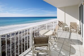 A balcony with white railings, wicker chairs, and a small table, overlooking a beach with white sand and clear blue water. - GD 603: Coastal Coolness - Get Hooked on Beach Living! (Fort Walton Beach)