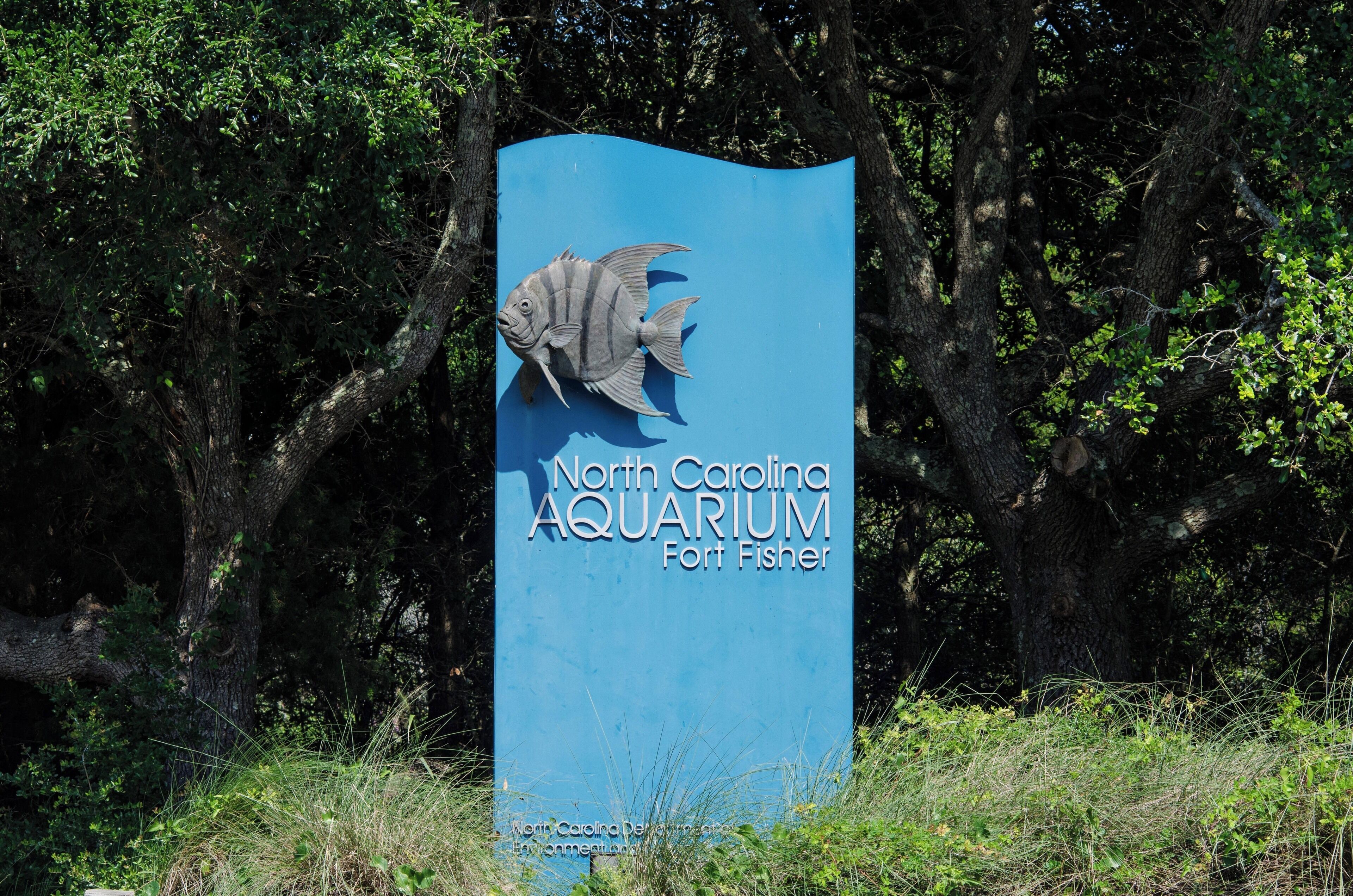 A blue sign with a fish and the text "North Carolina Aquarium Fort Fisher".