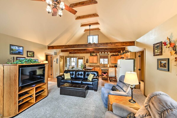 A spacious living area with a large TV, leather sofa, and a dining area with wooden beams and a kitchen in the background.