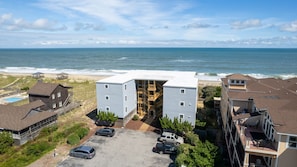 A coastal building with a large central entrance, adjacent parking, and a view of the ocean. - Enjoy Ocean Views and the Sound of Waves at Balcony Beach at Sea Oats (Kill Devil Hills)