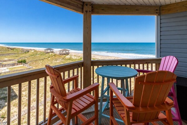 A wooden deck with a view of the beach and ocean. There are two Adirondack chairs and a small round table. - Enjoy Ocean Views and the Sound of Waves at Balcony Beach at Sea Oats (Kill Devil Hills)