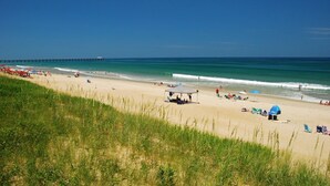 Ein Strand mit einem Pier im Hintergrund, klarem Himmel und Menschen, die sich am Strand erfreuen.
