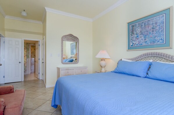 A bedroom with a large bed, a dresser, a mirror, a lamp, and a painting on the wall.