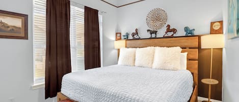 A bedroom with a bed, a bench, a ceiling fan, a bedside lamp, and a wall-mounted shelf with decorative items.