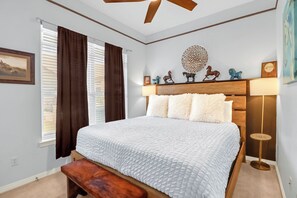 A bedroom with a bed, a bench, a ceiling fan, a bedside lamp, and a wall-mounted shelf with decorative items. - Amazing large home with Gorgeous Views, Swimming Pool, and Hot Tub (Wimberley)