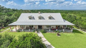 Une grande maison avec un toit en métal, une véranda et une pelouse bien entretenue.