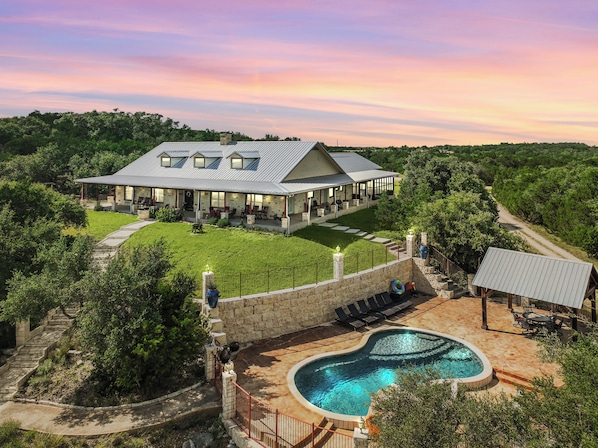A large house with a swimming pool, a covered patio, and a lawn.