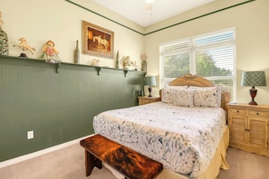 A bedroom with a bed, a bench, a nightstand, a lamp, and a window with blinds.