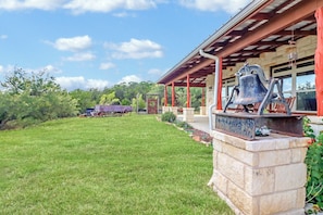 A building with a stone base, a porch with red pillars, and a bell sculpture.