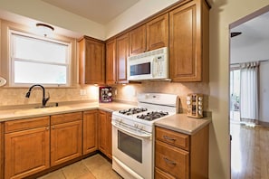 Una cocina con armarios de madera, estufa blanca, microondas y una ventana.