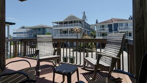 A wooden deck with outdoor furniture, including chairs and a table, overlooking a beachfront area with houses. - Popular townhome in heart of Wrightsville Beach! (Wrightsville Beach)