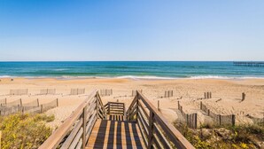 A wooden boardwalk leading to a sandy beach with a clear blue sky and ocean.