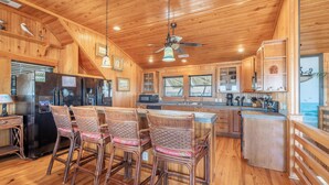 A wooden cabin interior with a kitchen, dining area, and bar seating.