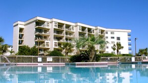 A hotel with a swimming pool, multiple balconies, and palm trees. - Direct Ocean & Beach View -Litchfield, Rare 2 Oceanfront Porches! (Pawleys Island)