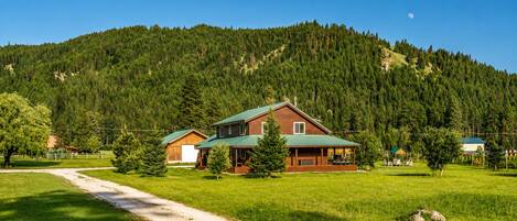 A cabin with a green roof, surrounded by a forested hillside.