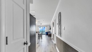 A hallway with a wooden floor, white walls, and a view to a balcony with a blue chair and table. - *20% Off New Summer 2026 Bookings* (Surfside Beach)