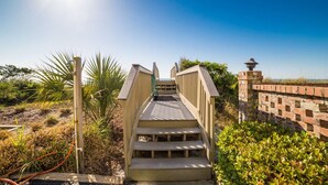 A wooden staircase leading to a beach area with a clear sky and a brick wall on the right. - *20% Off New Summer 2026 Bookings* (Surfside Beach)