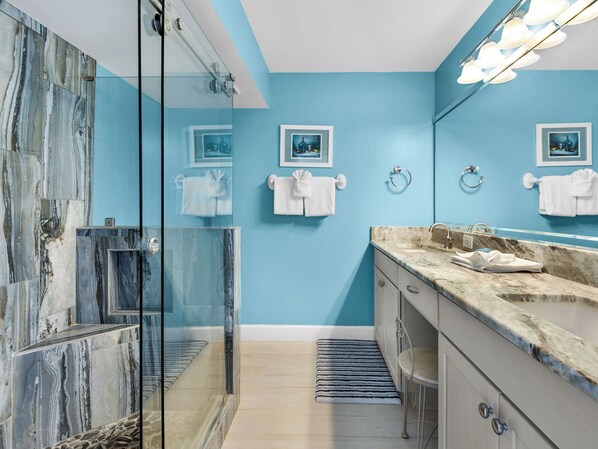 Une salle de bain moderne avec une douche à parois de verre, un lavabo en marbre et un mur d’accent bleu.